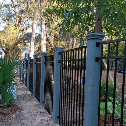 Black metal fence between painted columns beneath oak trees