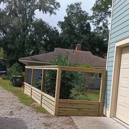 Wood-framed fence with wire infill and solid lower boards beside a driveway